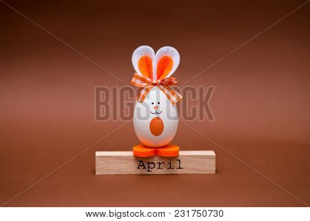 Multicolored Funny Eggs In The Form Of Cute Bunny With Wooden Calendar Set On April Isolated On Brow