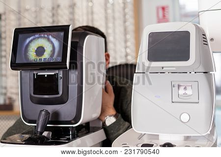 Ophthalmologist Examining Young Man With Optometric Machine In Optics Store