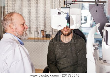 Ophthalmologist Examining Young Man With Optometric Machine In Optics Store