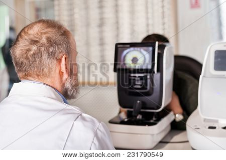 Ophthalmologist Examining Young Man With Optometric Machine In Optics Store