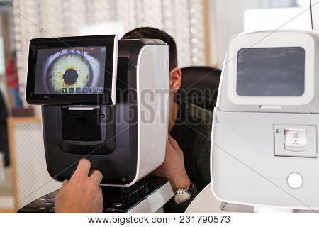 Ophthalmologist Examining Young Man With Optometric Machine In Optics Store