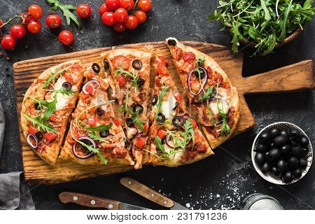 Flatbread Pizza Garnished With Fresh Arugula On Wooden Pizza Board, Top View. Dark Stone Background