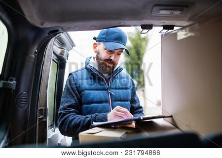 Delivery Man Delivering Parcel Box To Recipient - Courier Service Concept. A Man Signing A Document.