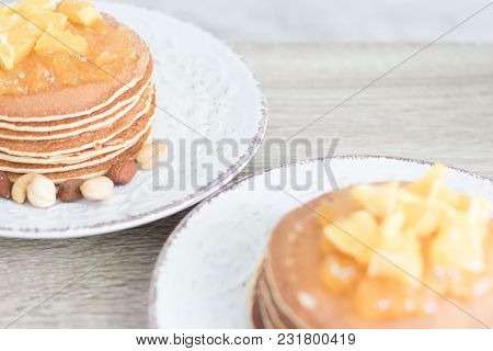 2 White Patterned Plates With Pancakes And Orange Jam And Nuts On Wooden Table Background. Closeup. 