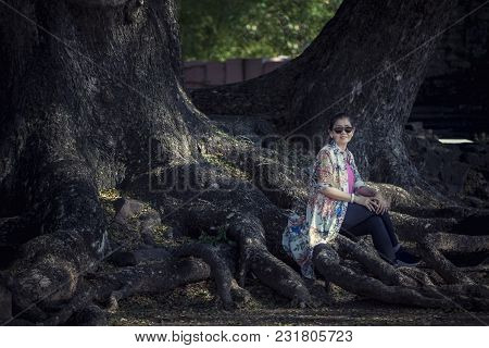 Asian Woman Sitting On Big Rain Tree Root In Traveling Destination