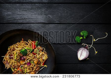 Udon Stir Fry Noodles With Meat Or Chicken And Vegetables In Wok Pan On Black Wooden Background. Top