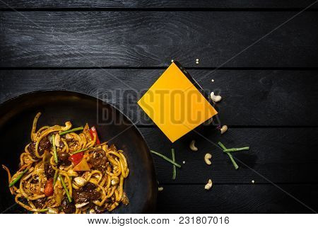 Udon Stir Fry Noodles With Meat And Vegetables In Wok Pan On Black Wooden Background. With A Box For