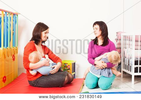 Two Mothers Are Brestfeeding Their Toddlers At The Playroom. Women Friendship