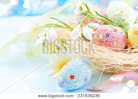 Easter colorful eggs background. Beautiful colorful eggs with decorations over blue wooden background, border design in pastel colors. Spring Flowers, holiday ribbon and painter eggs in the nest