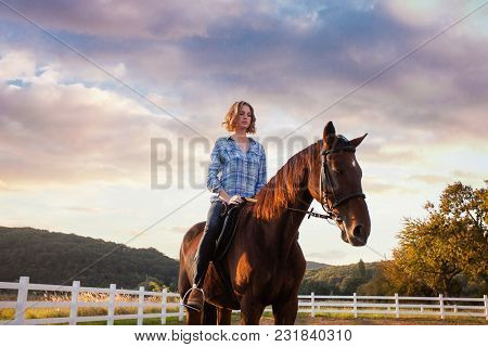 A Young Woman Riding A Horse Looks At The Sunset