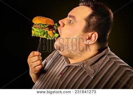 Diet failure of fat man eating fast food hamberger. Happy smile overweight person who spoiled healthy food by eating huge hamburger on fork. Junk meal leads to obesity. Use of harmful products.