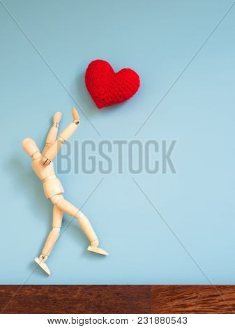 Wooden Puppet Jumping From The Wooden Floor In The Air To Catch The Red Heart Floating In The Sky. W