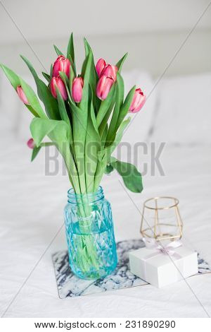 Home Interior. Bedroom. A Bouquet Of Tulips In A Glass Vase, A Candle, A Tray, A Box With A Gift Sta