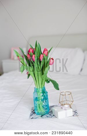 Home Interior. Bedroom. A Bouquet Of Tulips In A Glass Vase, A Candle, A Tray, A Box With A Gift Sta