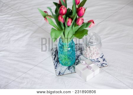 Home Interior. Bedroom. A Bouquet Of Tulips In A Glass Vase, A Candle, A Tray, A Box With A Gift Sta
