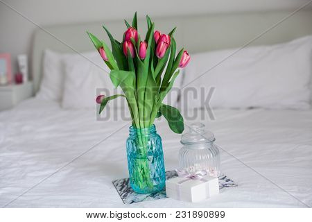 Home Interior. Bedroom. A Bouquet Of Tulips In A Glass Vase, A Candle, A Tray, A Box With A Gift Sta