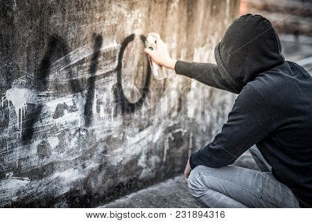 Mystery Man In Hoody Jacket Spraying Word No On The Wall In Abandoned Building. Anti Social Youth Ga