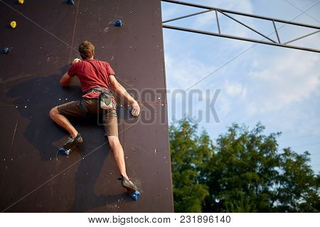 Sporty Man Practicing Rock Climbing In Climbing Gym Artificial Rock Training Wall Outdoors. Young Ta