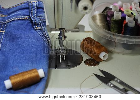 On The Table Of The Sewing Machine Lie Denim Fabrics, Close-up, Next To The Thread And Scissors.