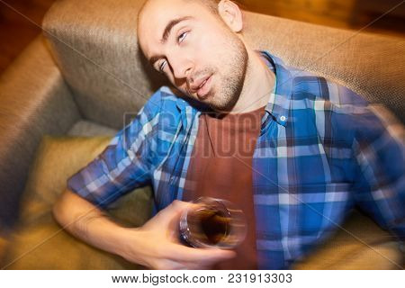 Man drunk. He is sitting on sofa and drinking alcohol