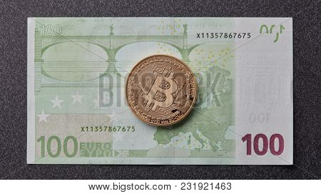 Gold bitcoin on one hundred euro banknote on a dark background