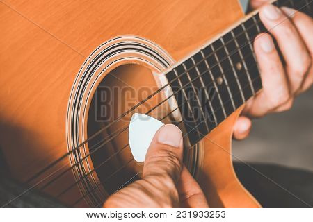 Hand Of Man Holding White Plectrum Playing Guitar