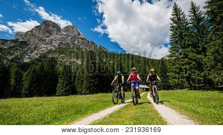 Tourist cycling in Cortina d'Ampezzo, stunning rocky mountains on the background. Family riding MTB enduro flow trail. South Tyrol province of Italy, Dolomites.