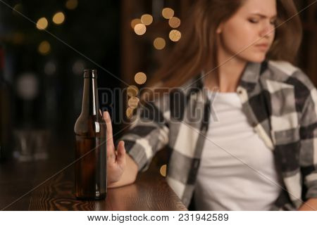 Young woman rejecting bottle of drink in bar. Alcoholism problem
