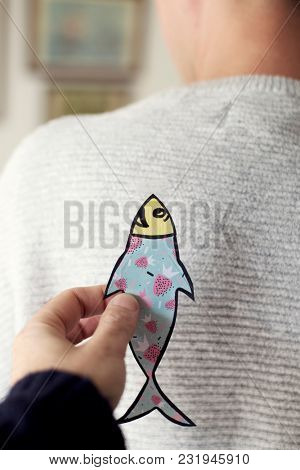 a young caucasian man seen from behind with a paper fish attached to his back, as a popular prank for april fools day in countries such as Italy, France, Belgium, Netherlands, Switzerland or Canada