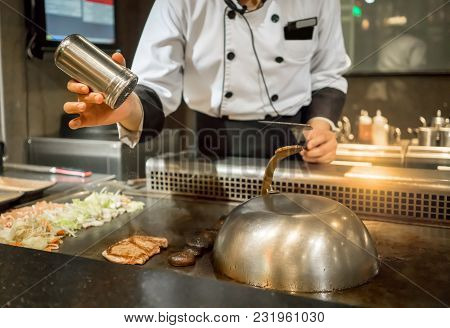 Hand Of Chef Adding Salt Into The Steak On Hot Pan In Front Of Customers. Japanese Tepanyaki Steak