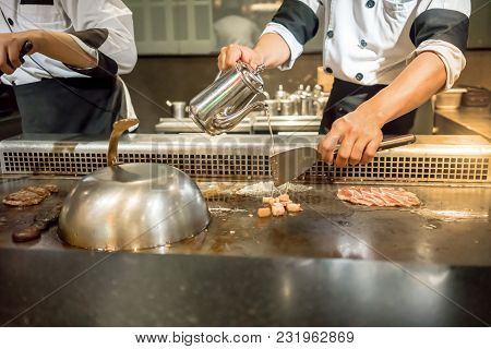 Hand Of Chef Adding Water Into The Steak On Hot Pan In Front Of Customers. Japanese Tepanyaki Steak