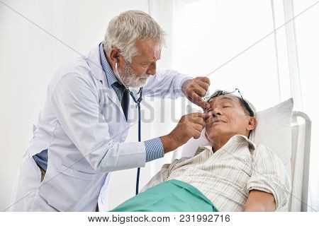 Senior Male Doctor Is Checking Asian Man Patient Eyes With In A Medical Room.