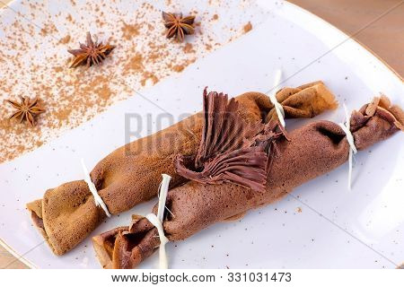 Chocolate Russian Pancakes, Blini With Curd Filling On The Plate. Served With A Chocolate Figure