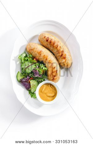 Top view of Bavarian sausages for frying with mustard sauce and mixed salad isolated. Traditional German rostbratwurst, wurst or bratwurst with fresh lettuce, rucola and chard leaves topview