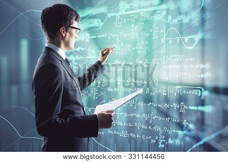 Attractive Young European Businessman With Mathematical Formulas Hologram On Blurry Office Interior 