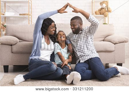 Adoption Concept. African American Foster Family Making Symbolic Roof Of Hands Gesture Above Little 