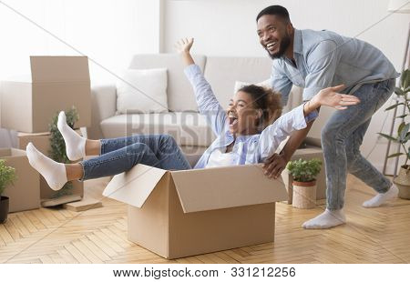 Excited African American Man Riding Woman In Cardboard Box Celebrating Moving Into New House. Select