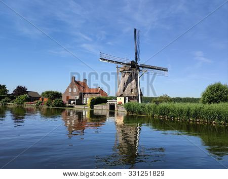 Canal Side View Of Hourse And A Windmill.