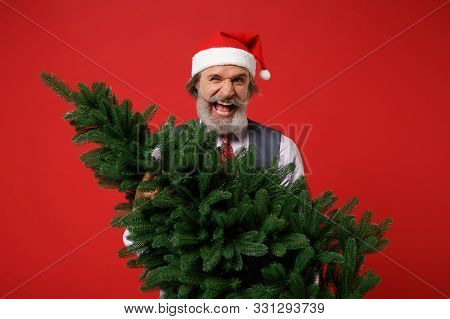 Crazy Funny Elderly Gray-haired Mustache Bearded Man In Santa Hat Shirt, Vest Tie Isolated On Red Ba