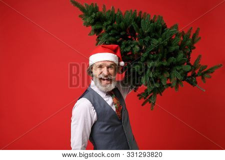 Crazy Funny Elderly Gray-haired Mustache Bearded Man In Santa Hat Shirt, Vest Tie Isolated On Red Ba