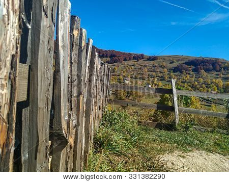 Old And Rustic Fence On The Side With Green Meadow And Small Mountain Houses In The Background On A 