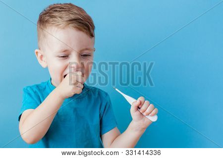 Ill Young Child With A Thermomether, Measuring The Height Of His Fever And Looking Into The Camera