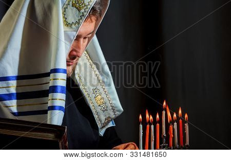 A Jewish Man In Prayer And Lighting Candles In A Menorah