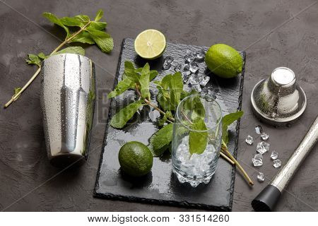 Set of bar tools: cocktail shaker, muddler and glass with ice, lime and mint  on dark stone  table. Top view. Bartender's tool. Mojito cocktail making.