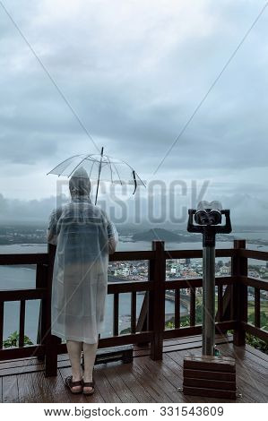 Man Standing In Raincoat Under Umbrella And Looking At Gloomy Skies