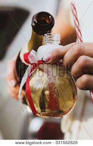 Female Hands Pouring Champagne Into A Light Bilb Shaped Party Glass Decorated With Red And White Rib