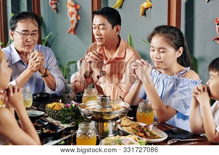 Vietnamese Family Members Closing Eyes When Praying Before Having Dinner At Home