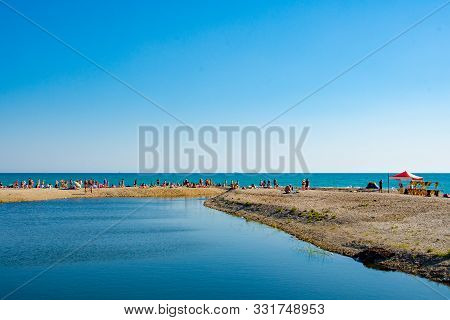 People On The Beach In The Summer. The River Flows Into The Sea.