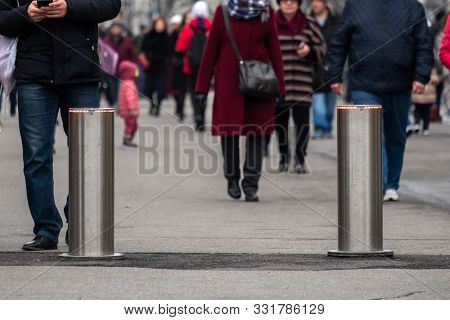 Automatic Cylindrical Barriers On The Pedestrian Zone Against The Background Of Blurry Feet Of Pedes