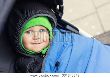 Portrait Of Cute Caucasian Toddler Boy In Black Hooded Warm Insulated Dawn Overall Jacket And Blue B